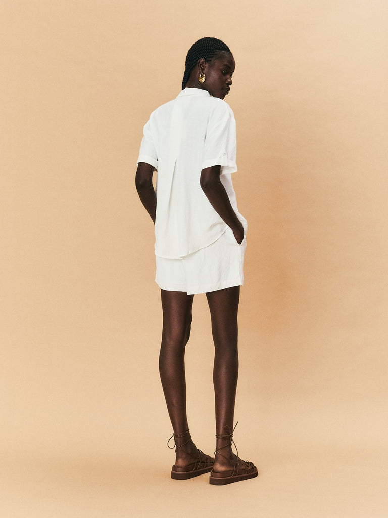 A young woman wearing La Maise shirt with white flower embroidery and La Maise Linen Shorts.