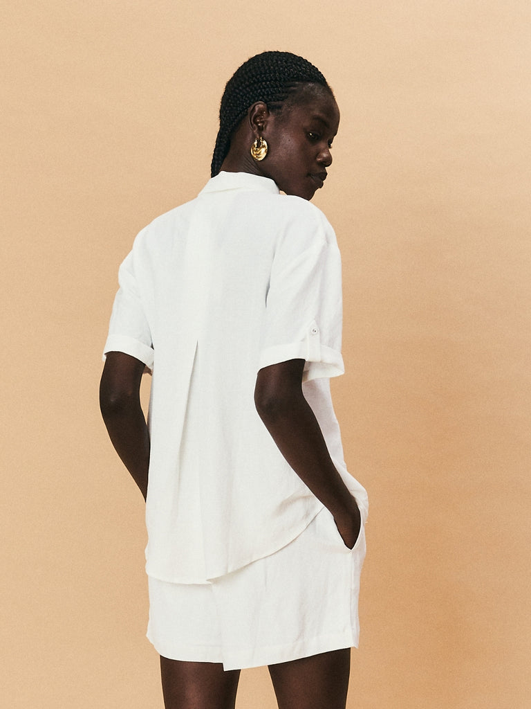 A young woman wearing La Maise Lillie shirt with white flower embroidery and La Maise linen shorts.