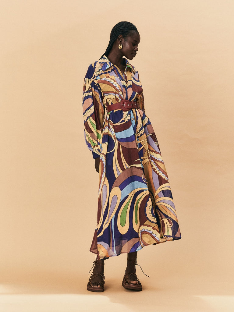 A woman wearing a colourful patterned La Maise Dijon Maxi Shirt Dress  against a beige background.