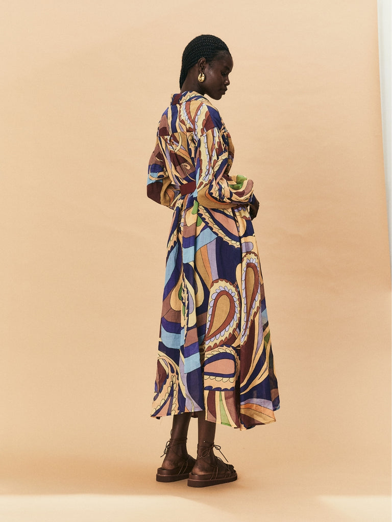 A woman wearing a colourful patterned La Maise Dijon Maxi Shirt Dress  against a beige background.