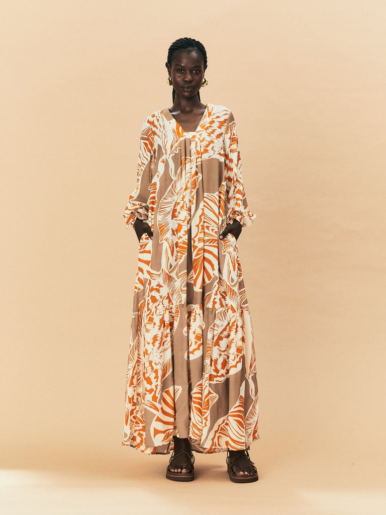 A young woman wearing a long, patterned La Maise dress against a beige background