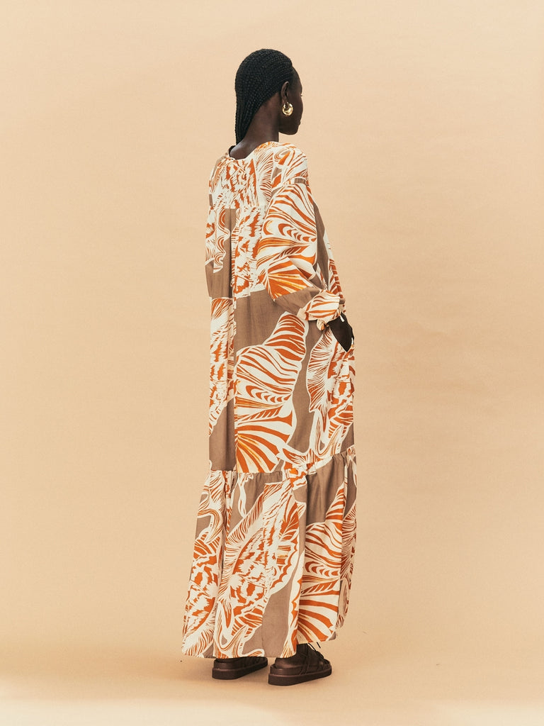 A young woman wearing a long, patterned La Maise dress against a beige background.
