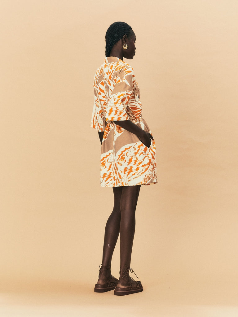 Person wearing a patterned dress with sheer overlay on a beige background