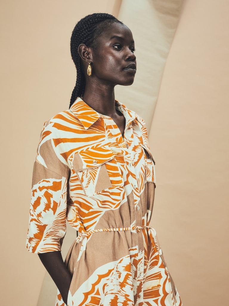 Woman wearing a patterned seashell print La Maise Cannes dress standing against a beige background.