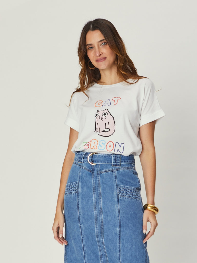 Woman wearing We Are The Others Jade Relaxed Tee – Cat Person, a white graphic T-shirt with playful cat print, styled with a denim skirt.