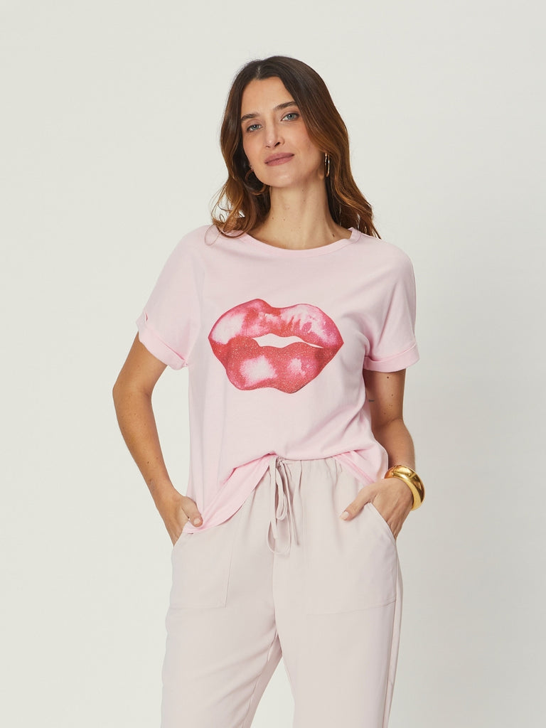 Woman wearing We Are The Others Jade Relaxed Tee – Lips Pink, a relaxed pink graphic T-shirt with bold lip print, styled with light pants.