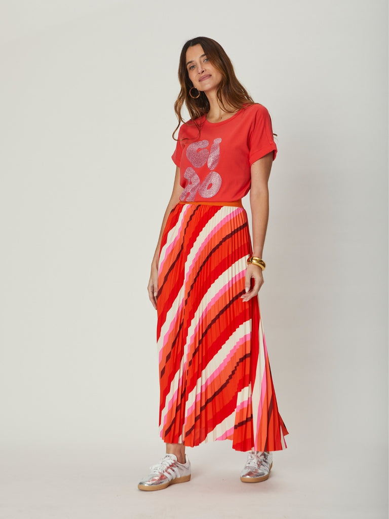 Woman wearing a red graphic WATO Chiao tee and a long red and white striped skirt on a plain background.