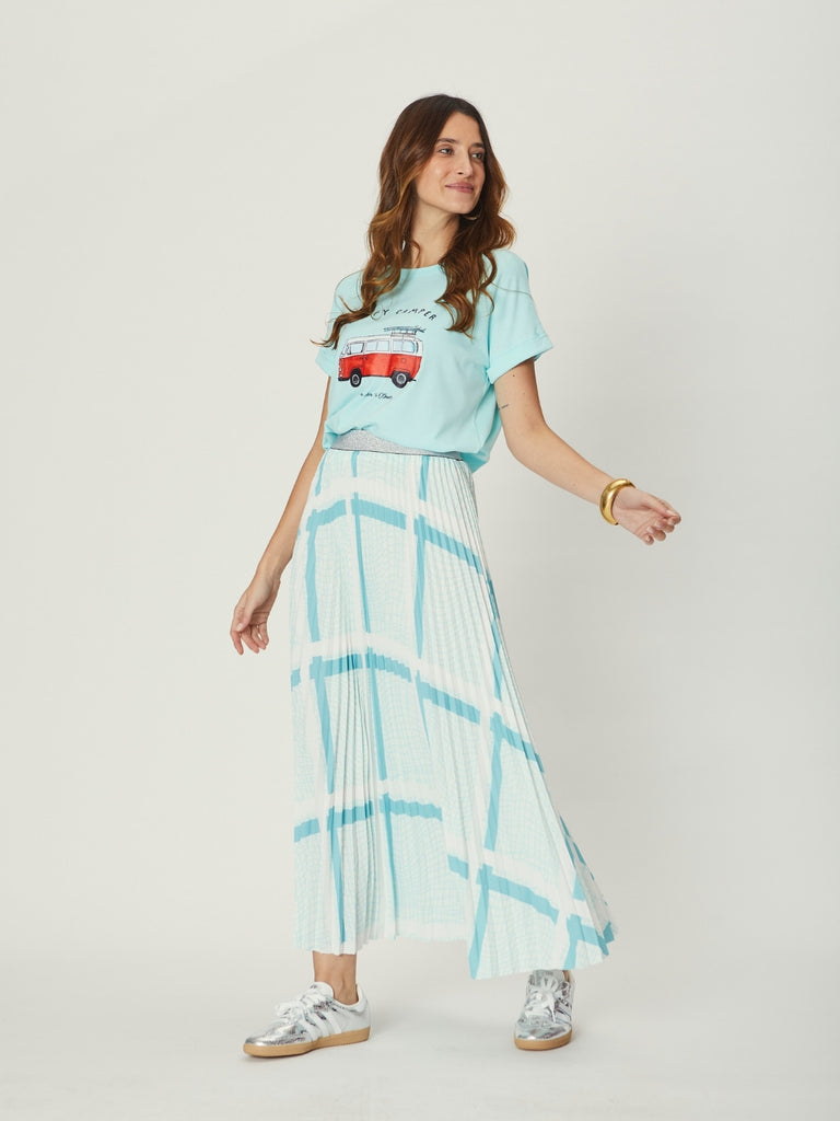 Woman wearing a light blue WATO graphic tee and a long plaid skirt on a white background