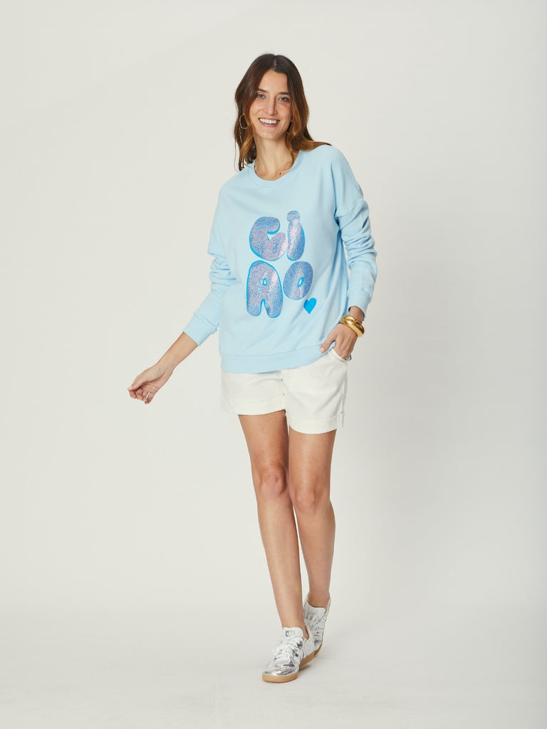 A woman wearing a light blue WATO sweater with 'GIRL' printed on it, standing against a plain background.