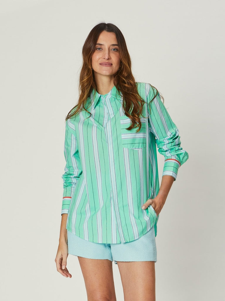 Model wearing the Chloe Shirt – Blue Stripe, a relaxed long-sleeve button-down with soft blue and white vertical stripes, chest pocket, and subtle red detailing