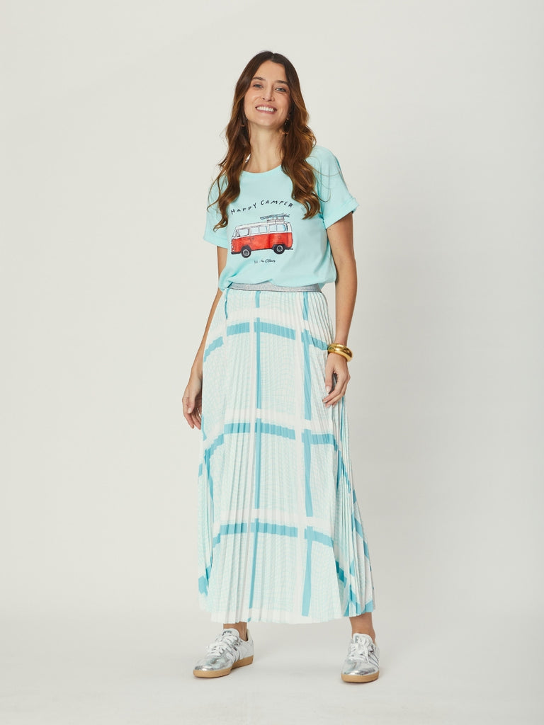 A woman wearing the Simone Pleat Skirt in teal base with a graphic tee, showcasing the skirt’s flowing pleated silhouette from the front