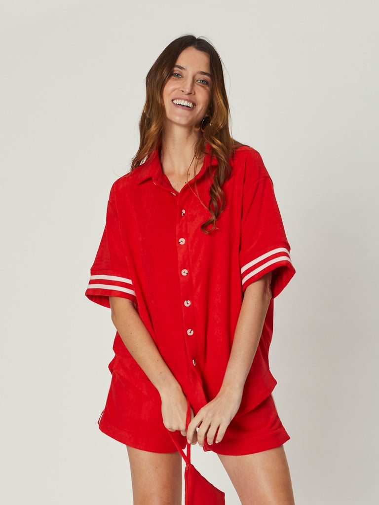 Model wearing the Stephanie Towelling Shirt in bold red, featuring a relaxed oversized fit, button-down front, and contrast sleeve stripes, styled with matching shorts.