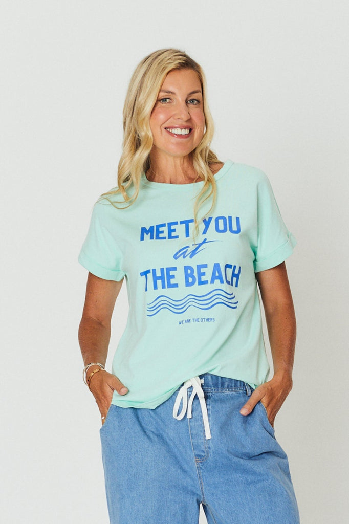Woman wearing a light green t-shirt with text and blue jeans on a white background