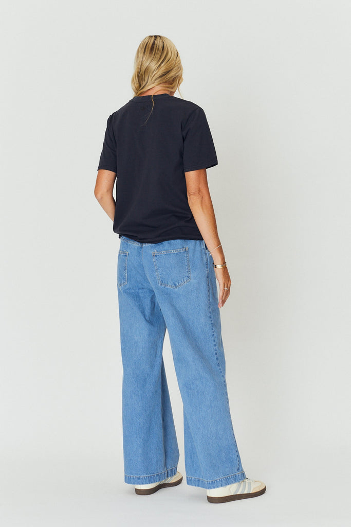Woman wearing a black t-shirt and blue jeans standing against a white background