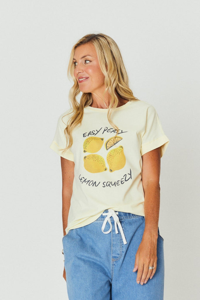 Woman wearing a graphic t-shirt and blue jeans standing against a white background
