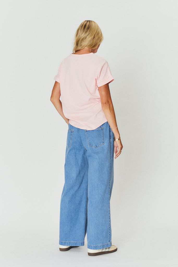 A view from the back, a woman wearing a light pink WATO tee with light blue denim pants.