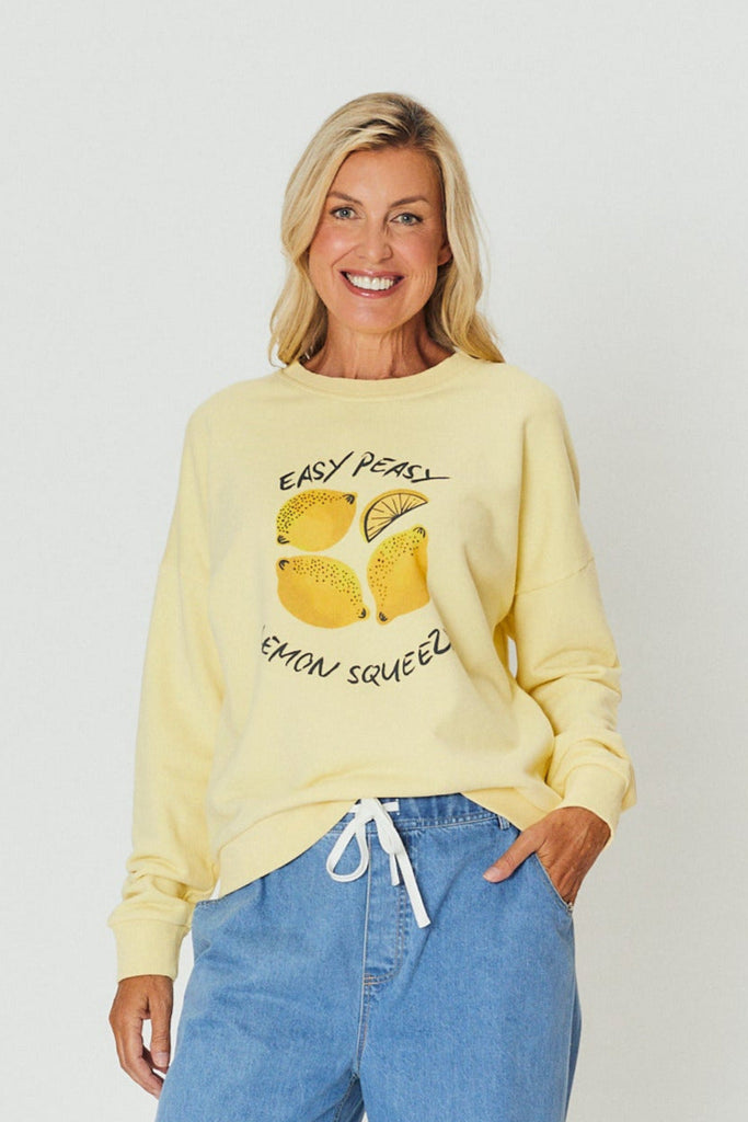 Woman wearing a yellow cotton sweatshirt with “Easy Peasy Lemon Squeezy” graphic print, styled casually with a light blue denim drawstring pants.