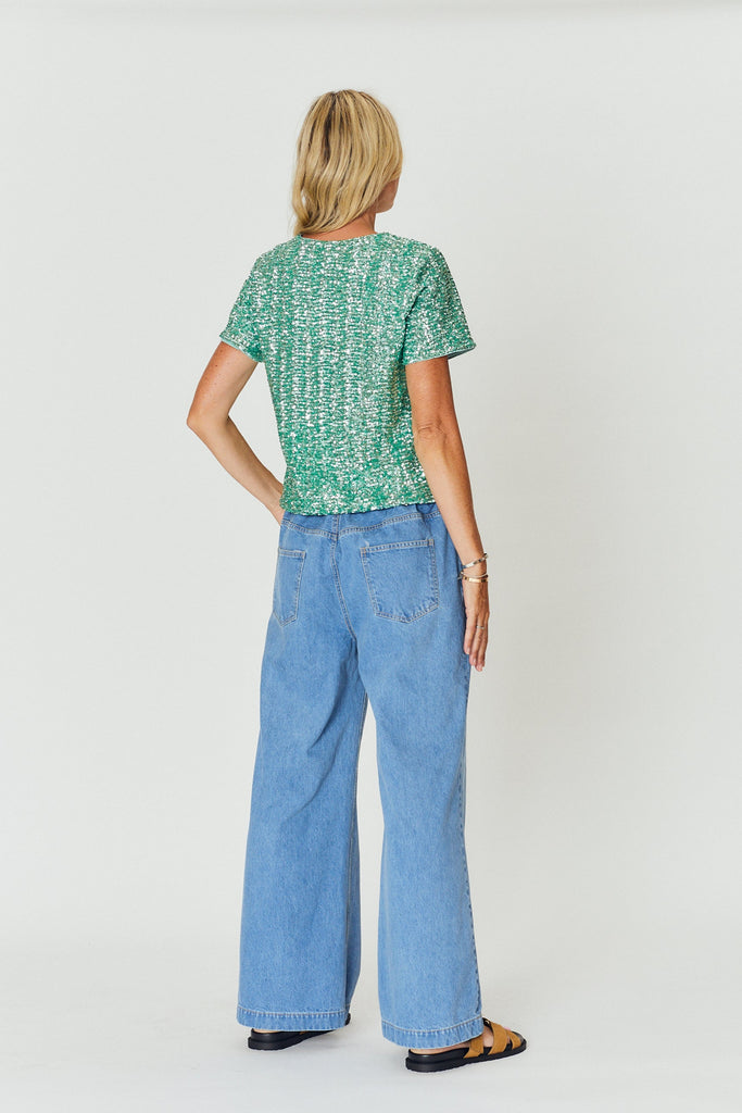 Woman wearing a green patterned top and blue jeans on a white background