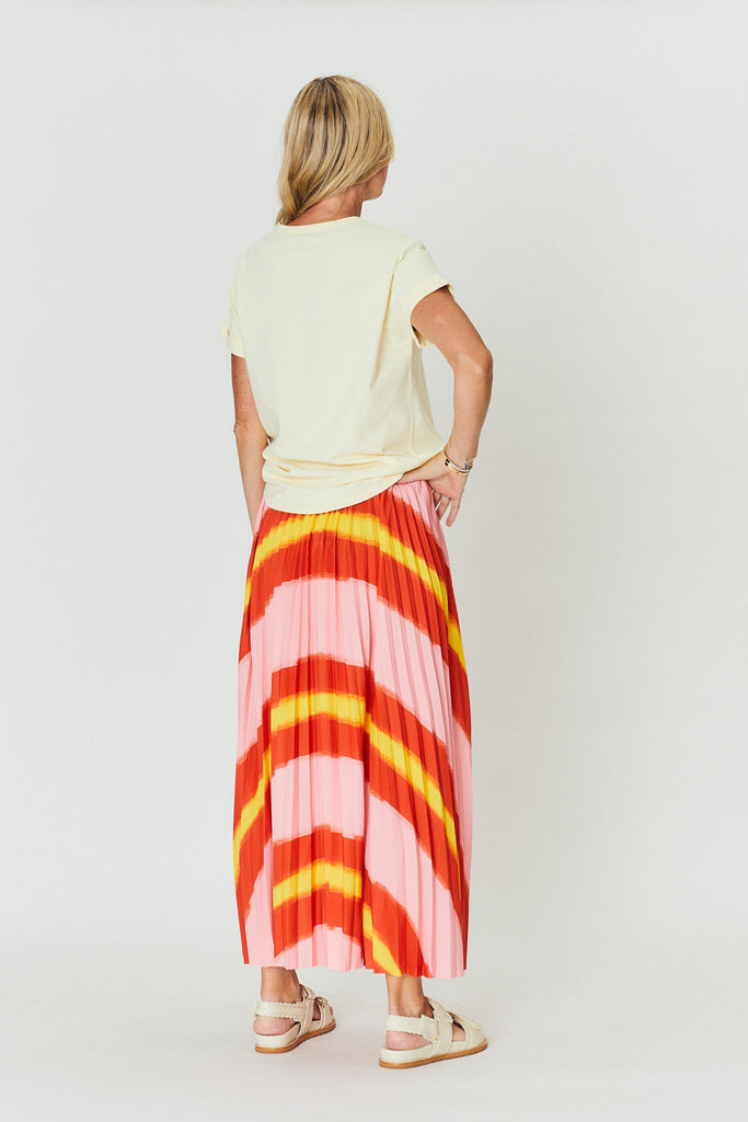 Woman wearing a white top and colorful pleated skirt on a white background