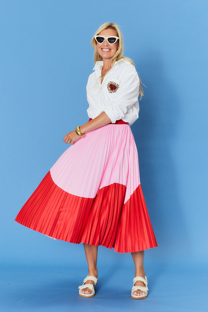 Woman wearing a white blouse and a pink and red pleated skirt on a blue background